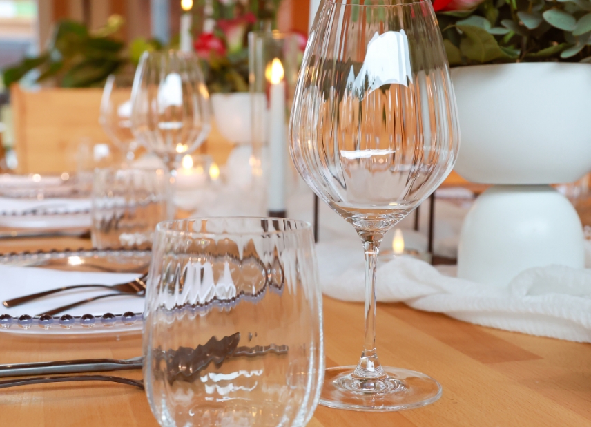 Close-up of a dining table set with empty wine glasses, plates, silverware, and a white floral centerpiece.