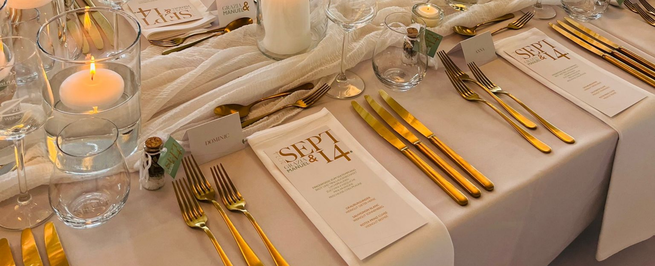 Elegant table setting with gold cutlery, clear glassware, white napkins, candles, and menu cards dated Sept 14.